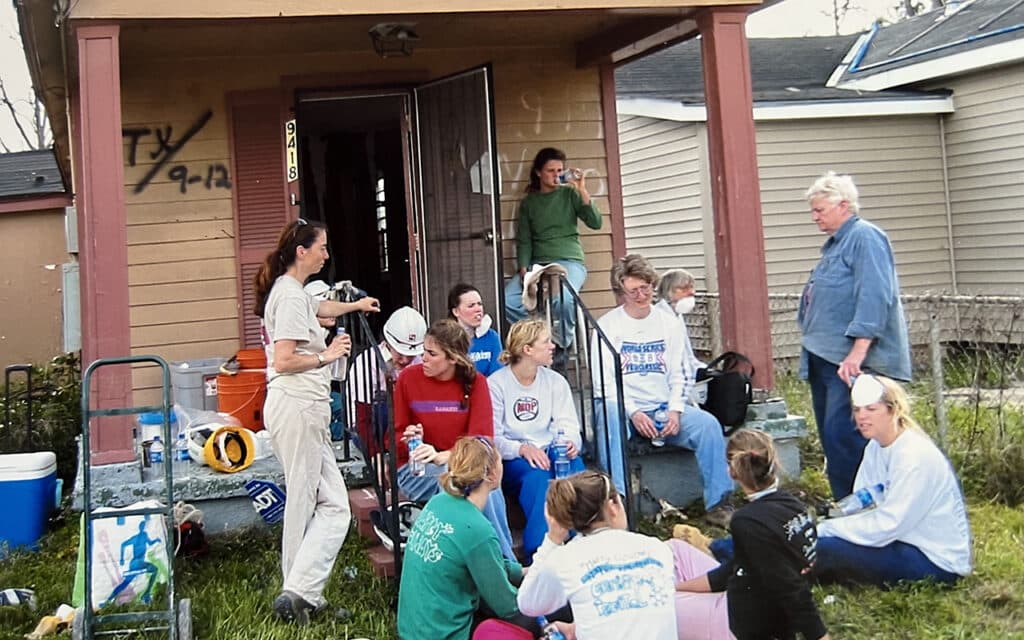 a group of volunteers sitting in front of a home damaged during Hurricane Katrina